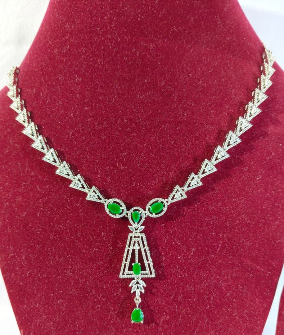 Elegant silver-tone necklace set featuring a line of clear stones, a geometric drop pendant with green gems, and matching earrings HJ43