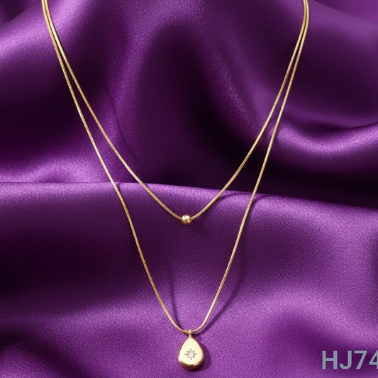 Gold double-layered chain necklace featuring a small bead and a teardrop pendant with a central starburst gem HJ74