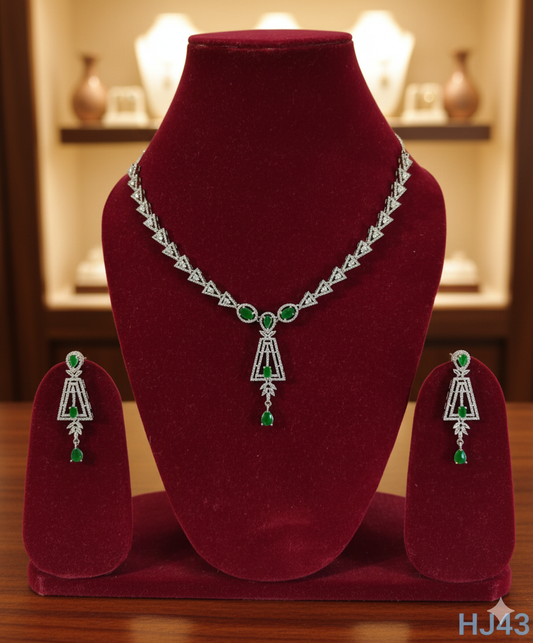 Elegant silver-tone necklace set featuring a line of clear stones, a geometric drop pendant with green gems, and matching earrings HJ43