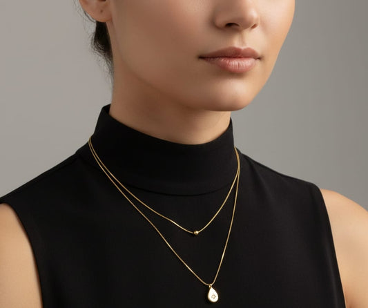Gold double-layered chain necklace featuring a small bead and a teardrop pendant with a central starburst gem HJ74